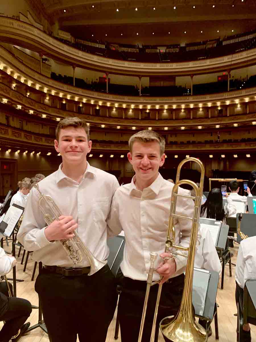 Tommy Roberts and Andrew Roberts at Carnegie Hall, side by side, each with an arm around the other, holding their instruments.