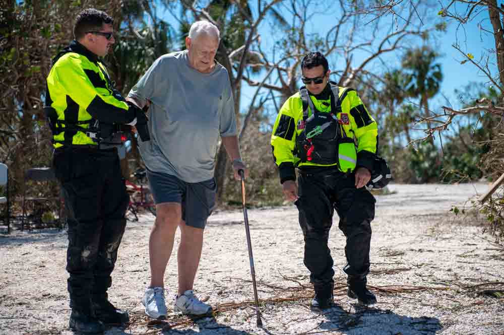 Members of the coast guard assisting an elderly man walking with a cane stranded on Sanibel Island,