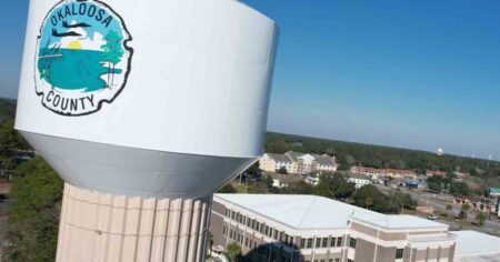 Aerial view of Okaloosa County water tower with county logo in foreground on the left, county administration building on right below.