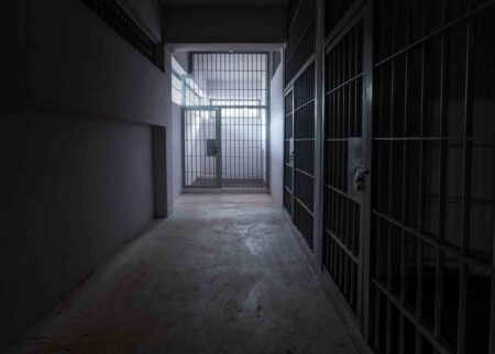 prison cells, one centered in hallway, lighted, and two darker cells on the right