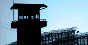 prison tower in shadows, fence topped with barbed wire.