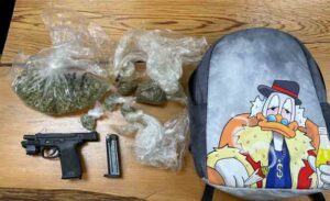 Clear plastic bags of marijuana, a handgun, and a backpack with a cartoon duck printed on it placed on a table.