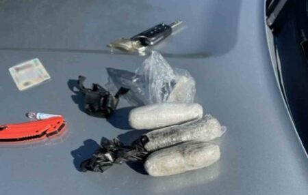 Rolled packages of cocaine, marijuana, driver license, and keys placed on the hood of a vehicle.