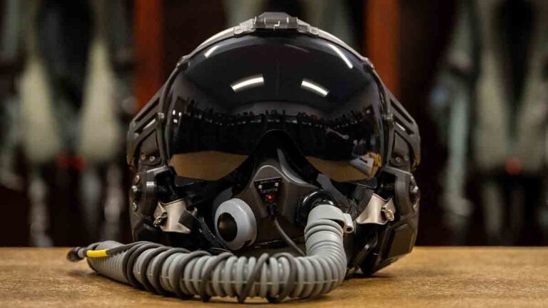 Air Force’s Next Generation Fixed Wing Helmet sits on a tabletop with flight suits hanging in the background