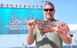 man holding lionfish with Lionfish Festival banner behind him.