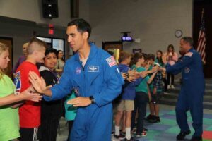 two astronauts slap hands with a line of young students.
