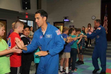 two astronauts slap hands with a line of young students.