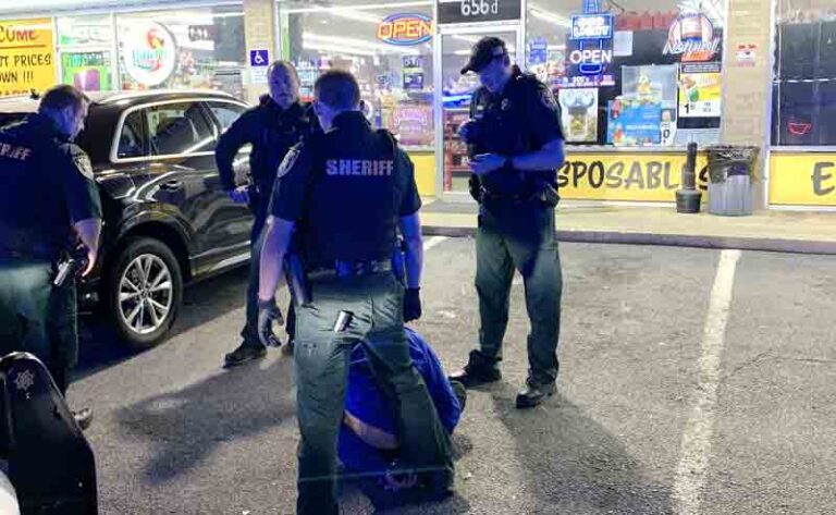 four deputies in store parking lot stand above a suspect who is kneeling