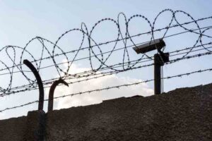 Security camera behind barbed wire fence on the wall, prison, security,