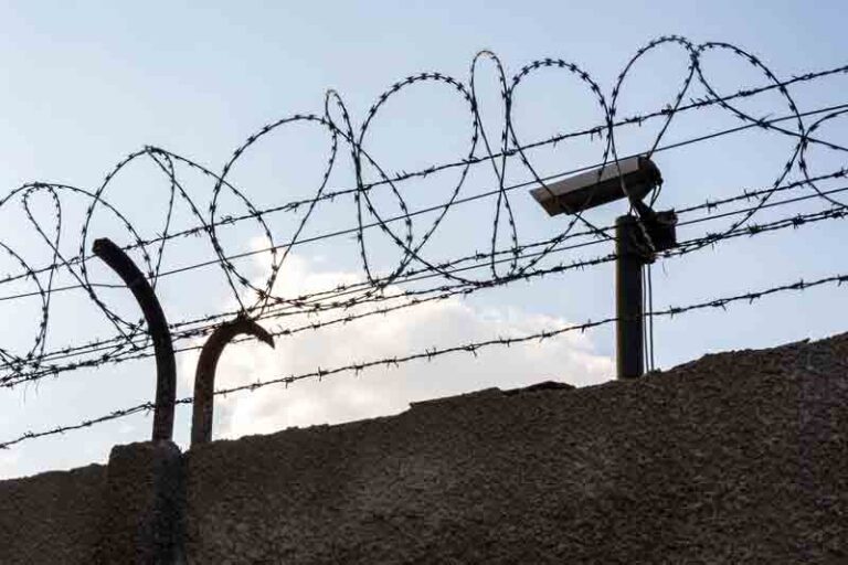 Security camera behind barbed wire fence on the wall, prison, security,