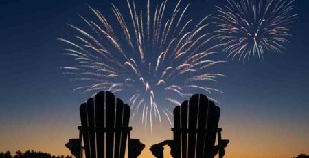 2 empty chairs on shoreline, fireworks in sky above