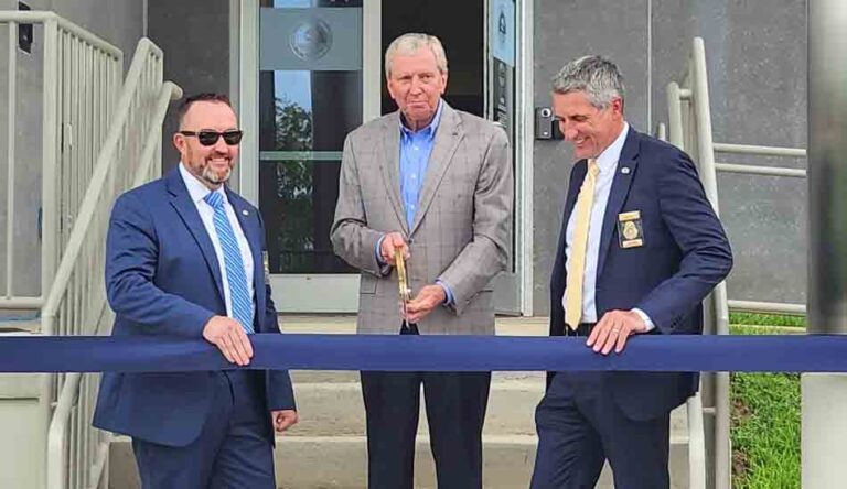 Three men prepare to cut a ceremonial ribbon.