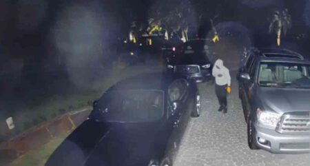 frame grab from a surveillance camera showing a suspect in a driveway with three vehicles.
