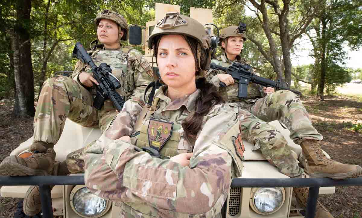 three female explosive ordnance disposal technician, two armed with weapons, pose with vehicle