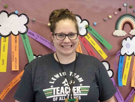 Bethany Culps in front of a colorful classroom bulletin board