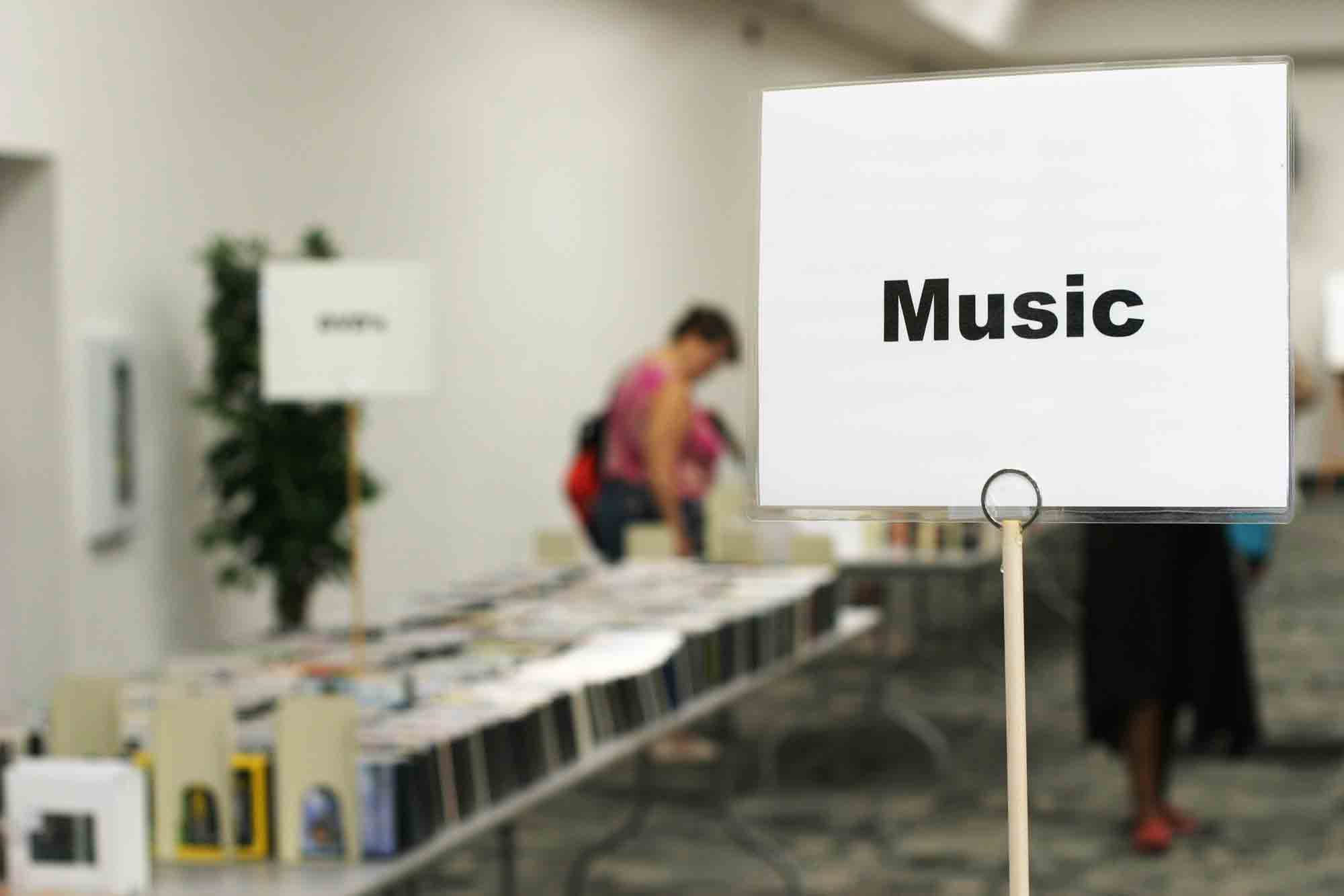 Sign reading "Music" with book sale patrons in the background