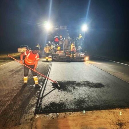 crew laying asphalt on a road bed at night