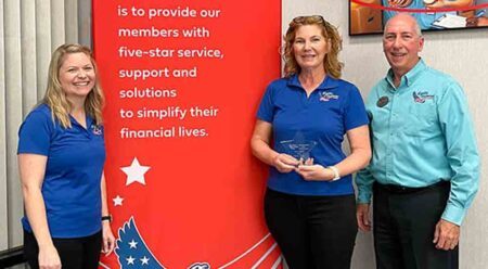two women and a man posing with an award standing next to indoor five-star service sign at credit union