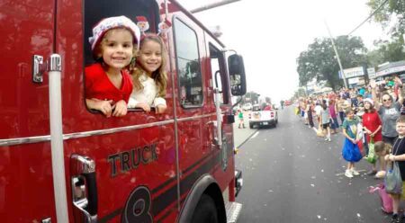 two smiling girls, one wearing a santa cap and the other wearing a santa hair head band, looking out from a fire truck in the 2022 Niceville Christmas Parade