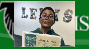 Omari Balbosa smiling, holding a Student of the Month award certificate