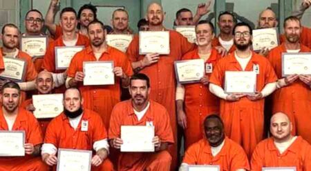 group of inmates in orange jumpsuits displaying graduation certificates