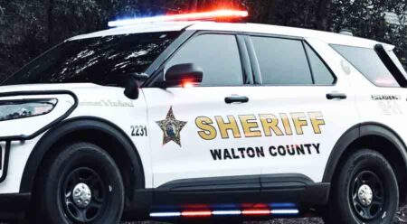 A parked Walton County Sheriff's Office patrol vehicle with red and blue lights flashing during the day