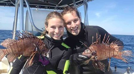 two divers in boat holding lionfish