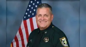 Head and shoulders portrait of Okaloosa County Sheriff Eric Aden in uniform with American flag behind his right shoulder