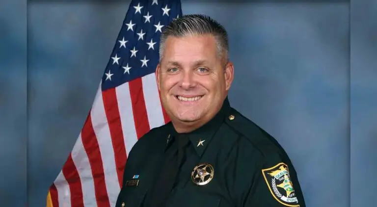 Head and shoulders portrait of Okaloosa County Sheriff Eric Aden in uniform with American flag behind his right shoulder