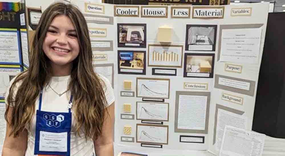 Emmalyn Otzenberger of the Okaloosa STEMM Academy standing in front of her science project display, cooler house, less material.