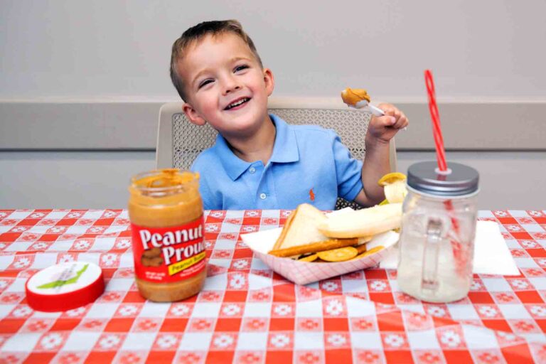 A boy seated at a table smiles as he prepares to enjoy a scoop of peanut butter