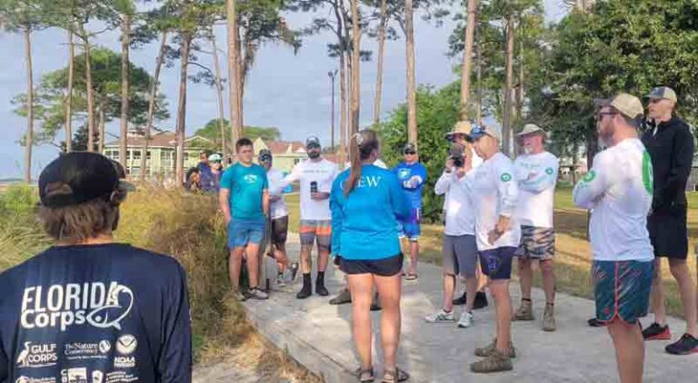 A group of volunteers with the Choctawhatchee Basin Alliance (CBA) and FORCE BLUE on a wood walk way near the shoreline.