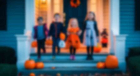 A group of children in Halloween costumes standing on a festively decorated porch, preparing to trick or treat.