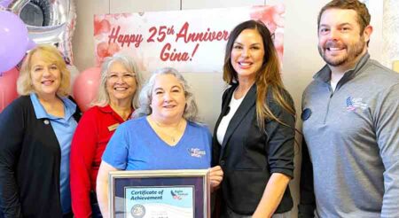 Close-up of a group of five celebrating a 25th work anniversary with a framed certificate.