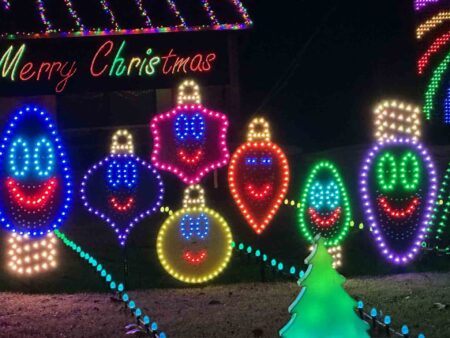 Smiling Christmas ornament-shaped light displays in a variety of colors, accompanied by a "Merry Christmas" sign at Geek Lights on the Corner.