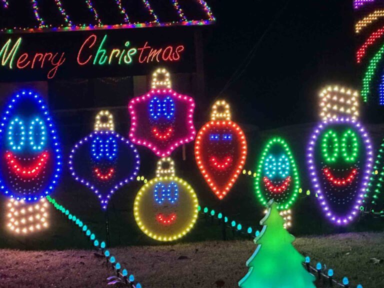 Smiling Christmas ornament-shaped light displays in a variety of colors, accompanied by a "Merry Christmas" sign at Geek Lights on the Corner.