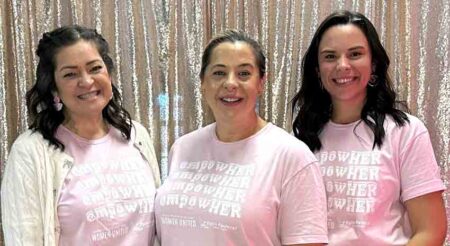 Close-up view of three women in pink shirts standing together at an event.