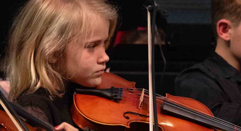 A focused young violinist from the Sinfonia Youth Orchestra performing during a concert.