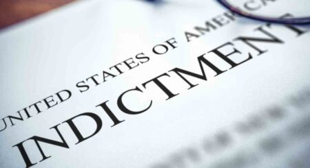 A United States federal indictment document with part of the heading visible and a pair of eyeglasses partially in frame.