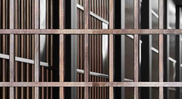 Close-up view of metal prison bars with dim lighting in the background.