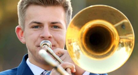 Close-up of Andrew Roberts playing the trombone outdoors, with the instrument's bell reflecting light.