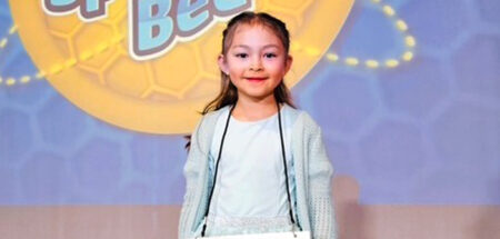 Vanessa Wesbur smiles in front of a spelling bee backdrop after competing.