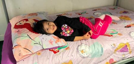 Young girl smiles while lying on a new bed with Disney princess bedding.