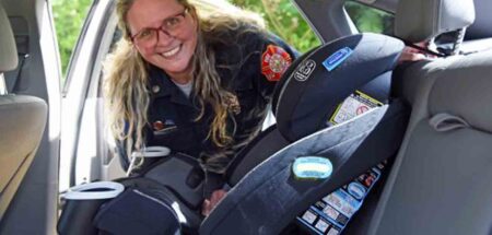 A Walton County Fire Rescue paramedic smiles while installing a child car seat in the backseat of a vehicle.