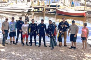 Group of scuba divers and volunteers posing on the beach at Bluewater Bay Marina before the underwater cleanup.