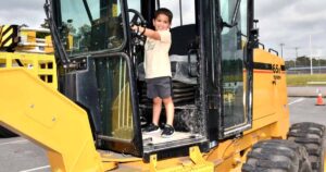 Smiling child standing in a construction vehicle at Big Truck Day.