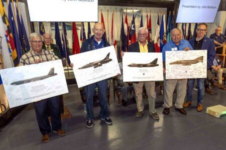 Vietnam veterans hold commemorative aircraft posters at tribute event