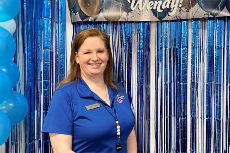 Wendy Ellerd stands smiling in front of blue and silver decorations during her 25-year recognition at Eglin Federal Credit Union.