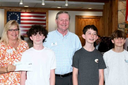 Kristi Evans, Mayor Henkel, and three students pose with a scholarship check in front of the Niceville City Council chambers.