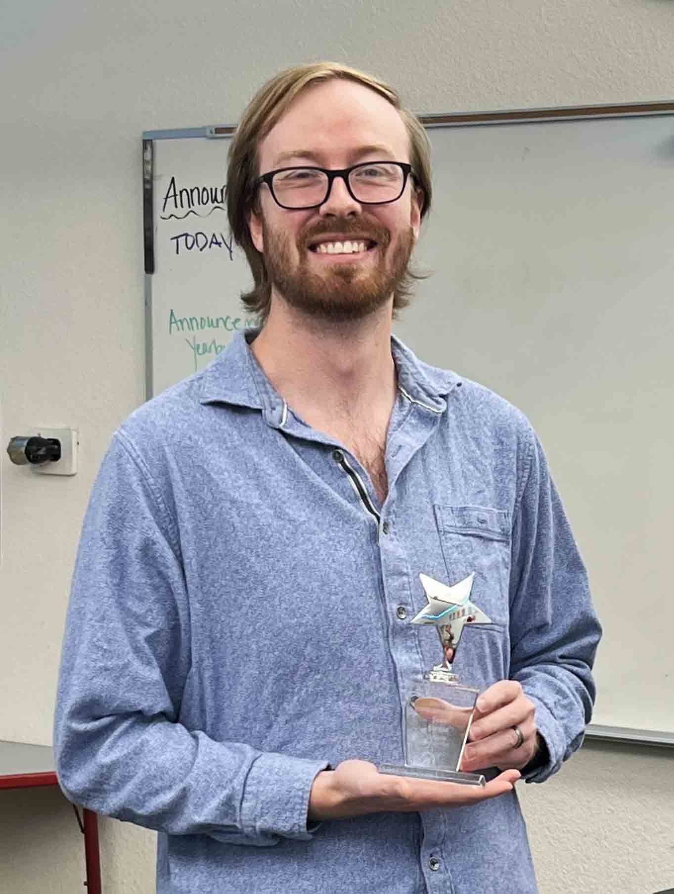 Sean Gordon smiles while holding a trophy in a classroom.